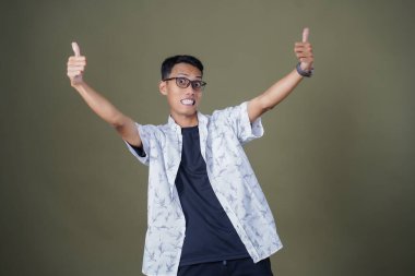 Gözlüklü, beyaz gömlekli, Asyalı bir adam. Mutlu bir şekilde baş parmak hareketi yapmak. Ordu yeşil arka planında izole edilmiş..