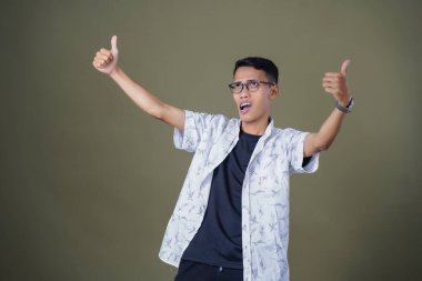 Gözlüklü, beyaz gömlekli, Asyalı bir adam. Mutlu bir şekilde baş parmak hareketi yapmak. Ordu yeşil arka planında izole edilmiş..