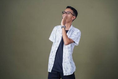 Heyecanlı, şok olmuş ya da heyecanlı bir poz. Ağızdan ağıza bağırıyordu. Gözlüklü, sıradan beyaz tişörtlü Asyalı bir adam askeri yeşil arka planda izole edilmiş...