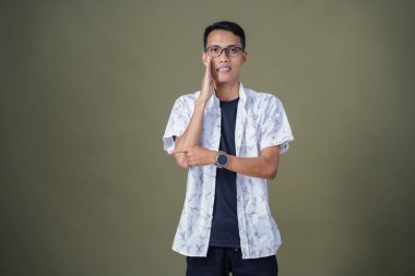 Heyecanlı, şok olmuş ya da heyecanlı bir poz. Boş uzayın kenarını gösteren el işaretleriyle bağırıyorlar. Gözlüklü, sıradan beyaz tişörtlü Asyalı bir adam askeri yeşil arka planda izole edilmiş..