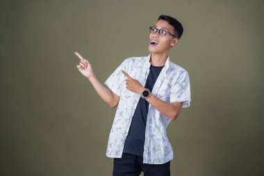 Heyecanlı, şok olmuş ya da heyecanlı bir poz. Boş uzayın kenarını gösteren el işaretleriyle bağırıyorlar. Gözlüklü, sıradan beyaz tişörtlü Asyalı bir adam askeri yeşil arka planda izole edilmiş..