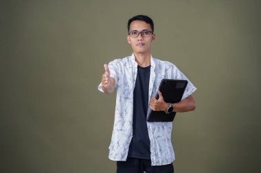 Gözlüklü, sıradan beyaz gömlek giyen Asyalı bir adam. Dostça selamlaşma ya da selam duruşu. Ordu yeşil arka planında izole edilmiş..