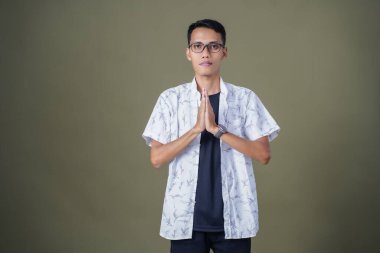 Gözlüklü, sıradan beyaz gömlek giyen Asyalı bir adam. Dostça selamlaşma ya da selam duruşu. Ordu yeşil arka planında izole edilmiş..