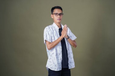 Gözlüklü, sıradan beyaz gömlek giyen Asyalı bir adam. Dostça selamlaşma ya da selam duruşu. Ordu yeşil arka planında izole edilmiş..