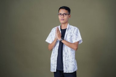 Gözlüklü, sıradan beyaz gömlek giyen Asyalı bir adam. Dostça selamlaşma ya da selam duruşu. Ordu yeşil arka planında izole edilmiş..