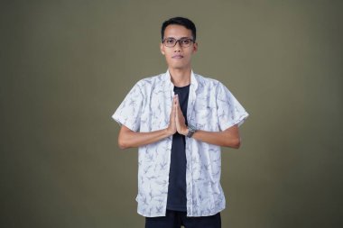 Gözlüklü, sıradan beyaz gömlek giyen Asyalı bir adam. Dostça selamlaşma ya da selam duruşu. Ordu yeşil arka planında izole edilmiş..