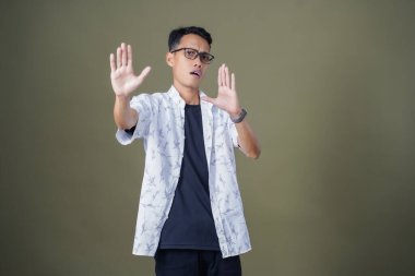 Gözlüklü genç Asyalı hayır, yasak, iyi bir jest yapmıyor. Ordu yeşil arka planında izole edilmiş..