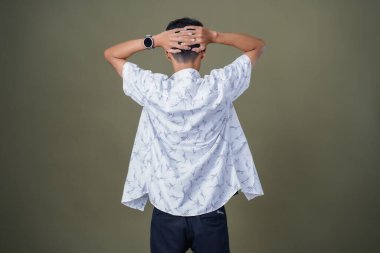 Asyalı genç adam başını tutarken arkaya bakıyor. Ordu yeşil arka planında izole edilmiş..