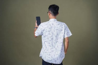 Arkadan akıllı telefon ekranına bakarken görülen genç adam. Ordu yeşil arka planında izole edilmiş..