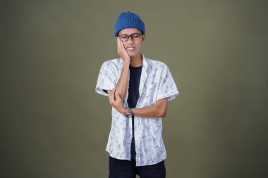 Gözlüklü, dişleri ağrıyan genç bir Asyalı. Ordu yeşil arka planında izole edilmiş..