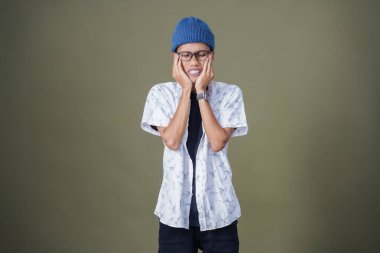 Gözlüklü, dişleri ağrıyan genç bir Asyalı. Ordu yeşil arka planında izole edilmiş..