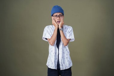 Gözlüklü, dişleri ağrıyan genç bir Asyalı. Ordu yeşil arka planında izole edilmiş..