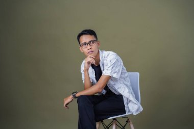 Gözlüklü genç Asyalı adam rahat rahat oturuyor. Ordu yeşil arka planında izole edilmiş..