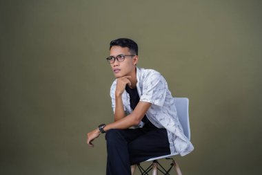 Gözlüklü genç Asyalı adam rahat rahat oturuyor. Ordu yeşil arka planında izole edilmiş..