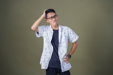 Gözlüklü, beyaz gömlekli, Asyalı bir adam. Baş döndürücü, sorunlu, üzgün bir ifade. Ordu yeşil arka planında izole edilmiş..