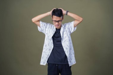 Gözlüklü, beyaz gömlekli, Asyalı bir adam. Baş döndürücü, sorunlu, üzgün bir ifade. Ordu yeşil arka planında izole edilmiş..