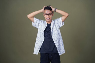 Gözlüklü, beyaz gömlekli, Asyalı bir adam. Baş döndürücü, sorunlu, üzgün bir ifade. Ordu yeşil arka planında izole edilmiş..