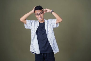 Gözlüklü, beyaz gömlekli, Asyalı bir adam. Baş döndürücü, sorunlu, üzgün bir ifade. Ordu yeşil arka planında izole edilmiş..