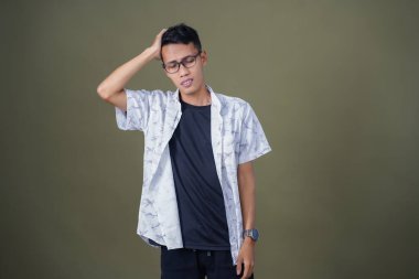 Gözlüklü, beyaz gömlekli, Asyalı bir adam. Baş döndürücü, sorunlu, üzgün bir ifade. Ordu yeşil arka planında izole edilmiş..