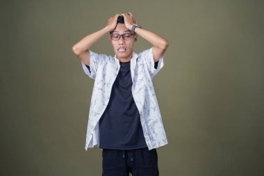 Gözlüklü, beyaz gömlekli, Asyalı bir adam. Baş döndürücü, sorunlu, üzgün bir ifade. Ordu yeşil arka planında izole edilmiş..