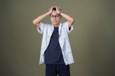 Gözlüklü, beyaz gömlekli, Asyalı bir adam. Baş döndürücü, sorunlu, üzgün bir ifade. Ordu yeşil arka planında izole edilmiş..