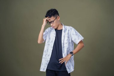 Gözlüklü, beyaz gömlekli, Asyalı bir adam. Baş döndürücü, sorunlu, üzgün bir ifade. Ordu yeşil arka planında izole edilmiş..