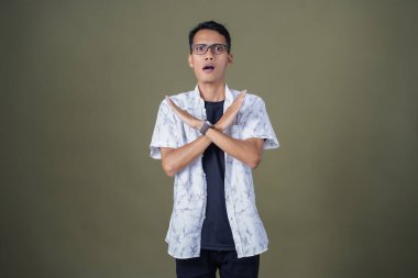 Gözlüklü genç Asyalı hayır, yasak, iyi bir jest yapmıyor. Ordu yeşil arka planında izole edilmiş..