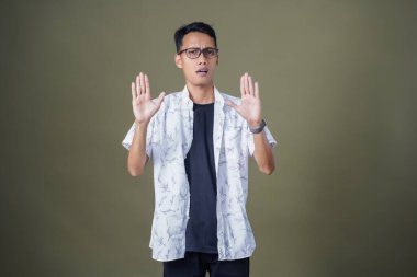 Gözlüklü genç Asyalı hayır, yasak, iyi bir jest yapmıyor. Ordu yeşil arka planında izole edilmiş..