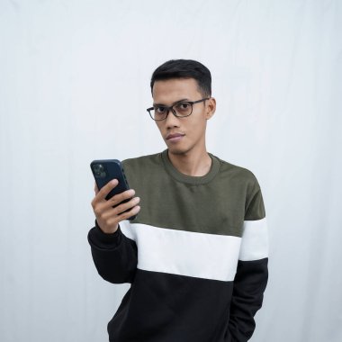 Akıllı telefon tutan gözlüklü, süveter giyen Asyalı genç bir adam. Beyaz arkaplanda izole.