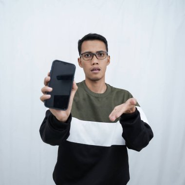 Gözlüklü, süveter giyen genç bir Asyalı akıllı telefon ekranını işaret ediyor. Beyaz bir arkaplanda izole edilmiş.