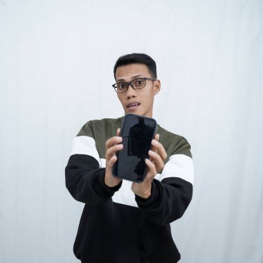 Gözlüklü, süveter giyen genç bir Asyalı akıllı telefon ekranını işaret ediyor. Beyaz bir arkaplanda izole edilmiş.