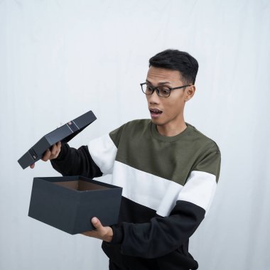 Gözlüklü Asyalı genç bir adam süveter giyiyor ve sürpriz bir hediye alıyor. Beyaz bir arkaplanda izole edilmiş.