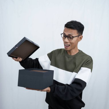 Gözlüklü Asyalı genç bir adam süveter giyiyor ve sürpriz bir hediye alıyor. Beyaz bir arkaplanda izole edilmiş.