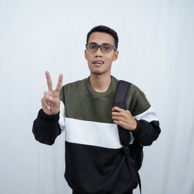 Hala okulda gözlüklü, süveter giyen ve çanta taşıyan genç bir Asyalı dik, havalı, gülümseyen bir poz veriyor. Beyaz bir arkaplanda izole edilmiş.