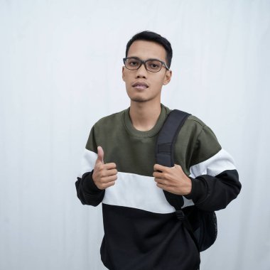 Hala okulda gözlüklü, süveter giyen ve çanta taşıyan genç bir Asyalı dik, havalı, gülümseyen bir poz veriyor. Beyaz bir arkaplanda izole edilmiş.