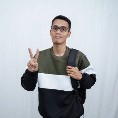 Hala okulda gözlüklü, süveter giyen ve çanta taşıyan genç bir Asyalı dik, havalı, gülümseyen bir poz veriyor. Beyaz bir arkaplanda izole edilmiş.