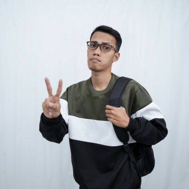 Hala okulda gözlüklü, süveter giyen ve çanta taşıyan genç bir Asyalı dik, havalı, gülümseyen bir poz veriyor. Beyaz bir arkaplanda izole edilmiş.