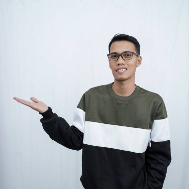 Gözlüklü, süveter giyen genç bir Asyalı boş bir yeri işaret ederken mutlu bir şekilde gülümsüyor. Beyaz bir arkaplanda izole edilmiş.