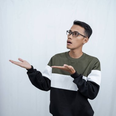 Gözlüklü, süveter giyen genç bir Asyalı boş bir yeri işaret ederken mutlu bir şekilde gülümsüyor. Beyaz bir arkaplanda izole edilmiş.