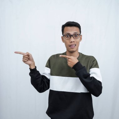 Gözlüklü, süveter giyen genç bir Asyalı boş bir yeri işaret ederken mutlu bir şekilde gülümsüyor. Beyaz bir arkaplanda izole edilmiş.