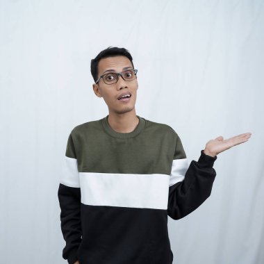 Gözlüklü, süveter giyen genç bir Asyalı boş bir yeri işaret ederken mutlu bir şekilde gülümsüyor. Beyaz bir arkaplanda izole edilmiş.