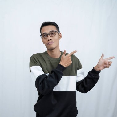 Gözlüklü, süveter giyen genç bir Asyalı boş bir yeri işaret ederken mutlu bir şekilde gülümsüyor. Beyaz bir arkaplanda izole edilmiş.