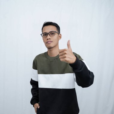 Gözlüklü, süveter giyen, gülümseyen ve işaret veren Asyalı genç bir adam. Beyaz arkaplanda izole.