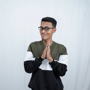 Gözlüklü Asyalı genç bir adam süveter giyiyor ve gizemli bir şeyler saklıyor. Ya da şeytani şeyler düşünüyor. Beyaz arkaplanda izole.