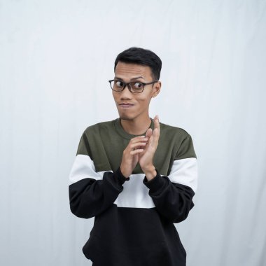 Gözlüklü Asyalı genç bir adam süveter giyiyor ve gizemli bir şeyler saklıyor. Ya da şeytani şeyler düşünüyor. Beyaz arkaplanda izole.