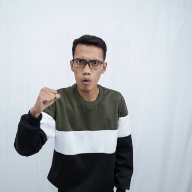 Gözlüklü, mutlu, heyecanlı ve muzaffer bir ifadeyle süveter giyen genç bir Asyalı yumruğunu kaldırıp sıkarken. Beyaz arkaplanda izole.