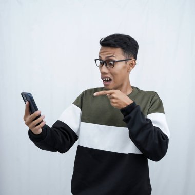 Gözlüklü, süveter giyen, mutlu bir ifadeyle akıllı telefona bakarken şaşıran genç bir Asyalı. Beyaz bir arkaplanda izole edilmiş.