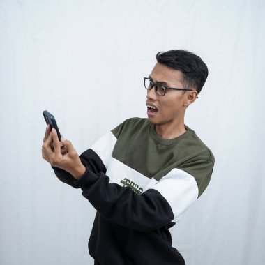 Gözlüklü, süveter giyen, mutlu bir ifadeyle akıllı telefona bakarken şaşıran genç bir Asyalı. Beyaz bir arkaplanda izole edilmiş.