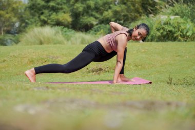 Zihinsel ve fiziksel sağlık. Sıska, bronz tenli Asyalı bir kız sabah sakin bir nehirde yoga yapıyor. Kadın, kollarını açmış savaşçı pozunda duruyor..