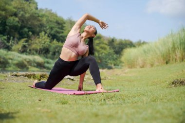 Zihinsel ve fiziksel sağlık. Sıska, bronzlaşmış, spor giyimli Asyalı bir kadın sabahın bu saatinde güzel bir nehir kenarında yoga yapıyor. Kadın Genişletilmiş Kenar Açı Pozu 'nu yapıyor..